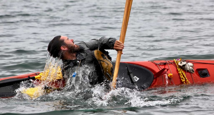 A person practices a wet exit in a kayak on a body of water. 